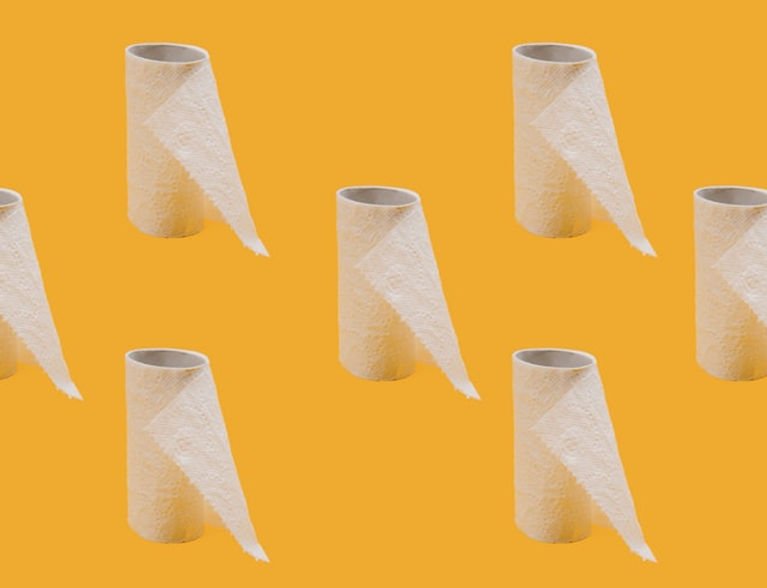 Toilet paper rolls with sheets, evenly spaced on a bright orange background, creating a playful and orderly pattern.