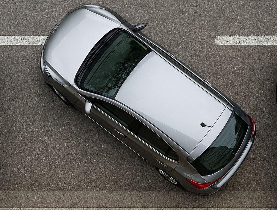 Silver car parked on a gray asphalt road, viewed from above. A white line is visible next to the car. Calm and neutral setting.